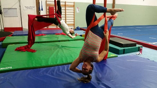 Two aerialists performing on two different hanging cloths in a room full of mats